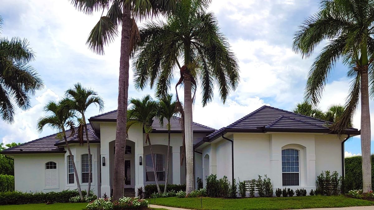 White stucco South Florida home with a dark flat-tile roof, arched windows and royal palms