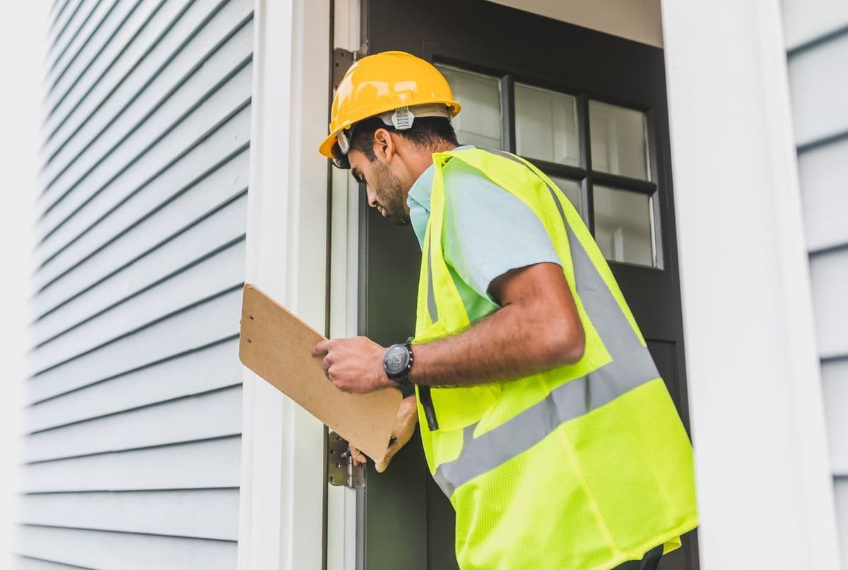 Contractor in a hard hat checking a door opening against a clipboard during a site inspection
