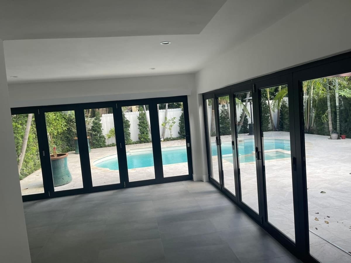 Wall of dark-framed folding glass doors opening a room to the pool